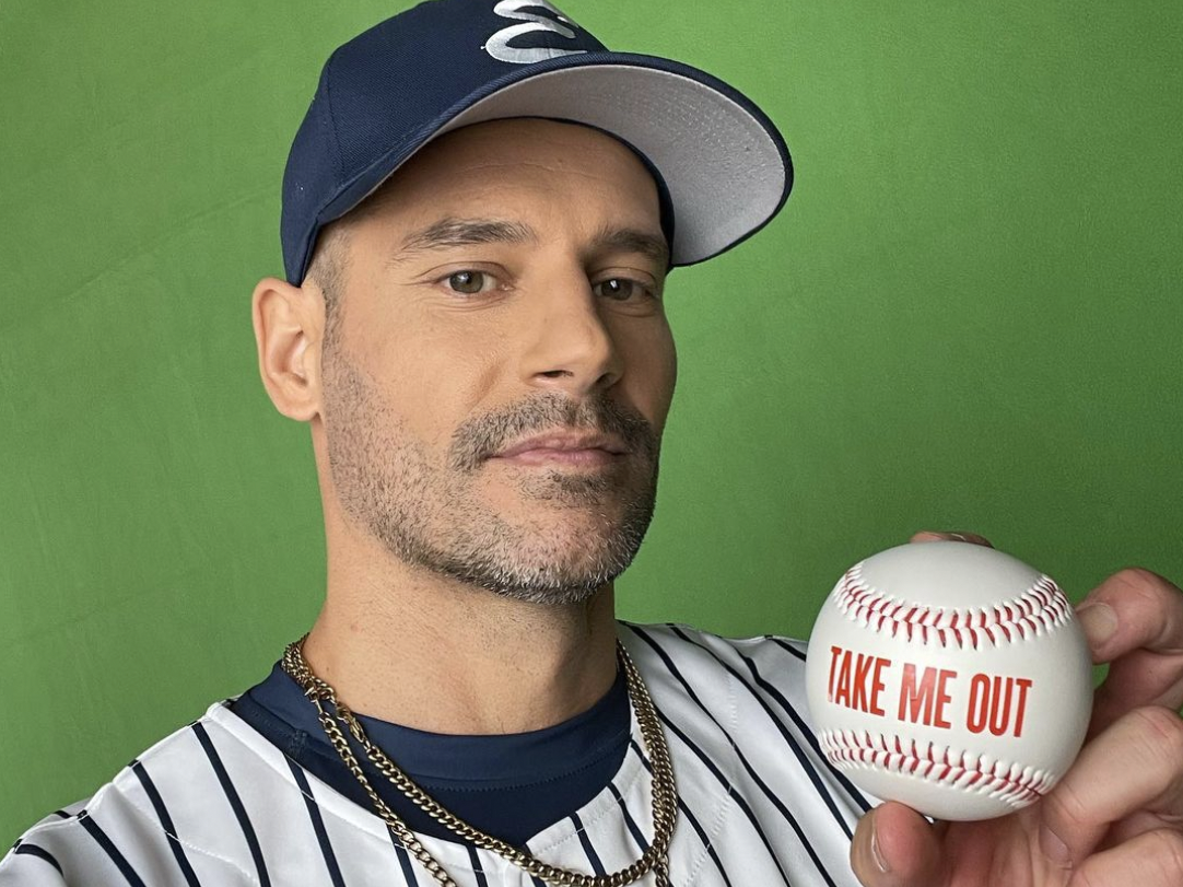 Baseball player who is taking a photo of himself holding a baseball that states Take Me Out