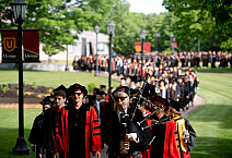Line of facility and students walking to their commencement ceremony dressed in proper cap and gown attire in an orderly fashion.
