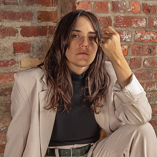 Headshot of Emily Wells sitting against a brick wall.
