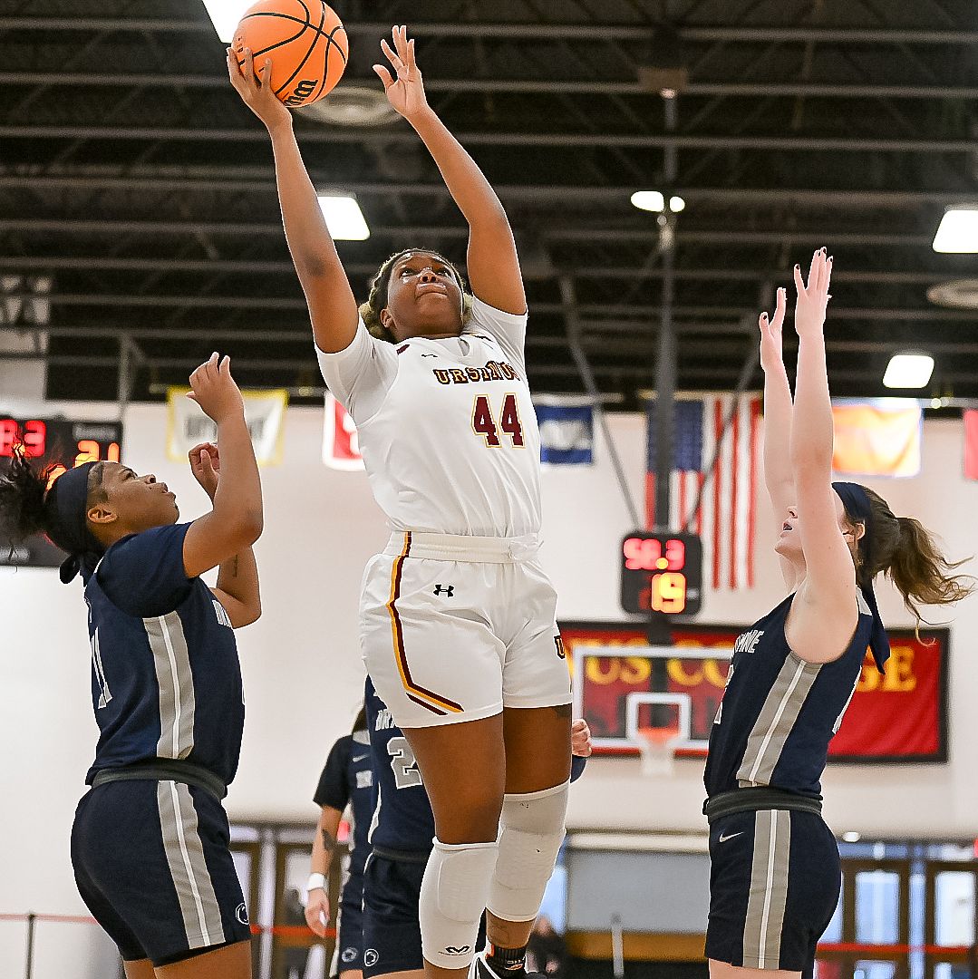 Support Women's Basketball 001 Ursinus College women's basketball player taking a shot with two defenders on either side.