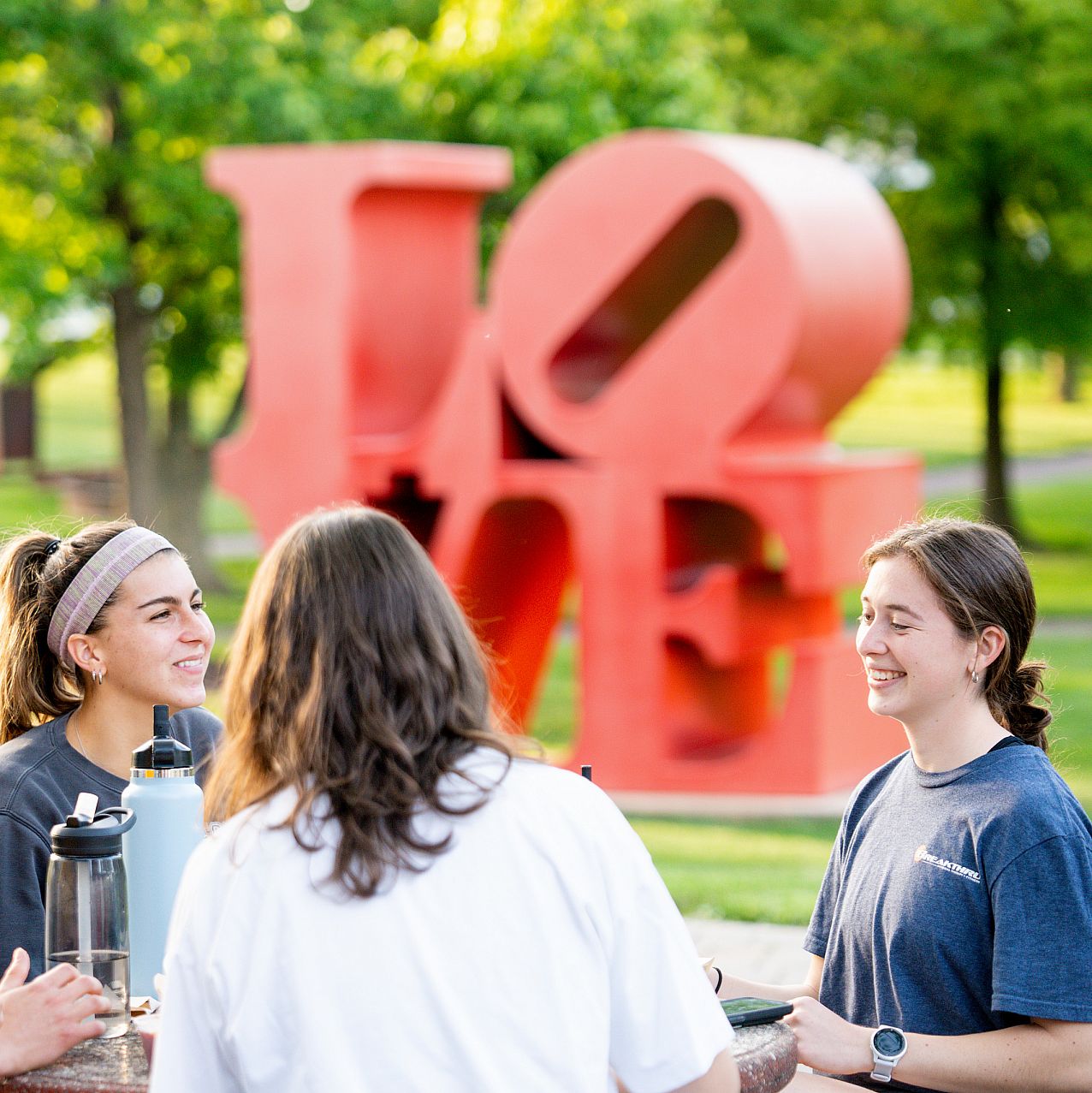 Student Candid w Love Statue Group of students sitting outside at table conversating.