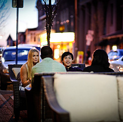 Group of people sitting on outside couch furniture in a city at night talking.